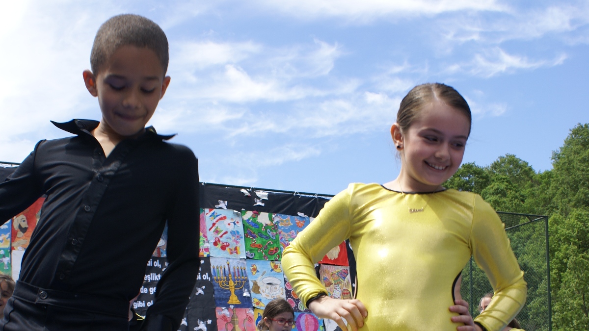 A close-up photo of a boy and a girl both around the age of ten on the stage in an open-air dance recital.