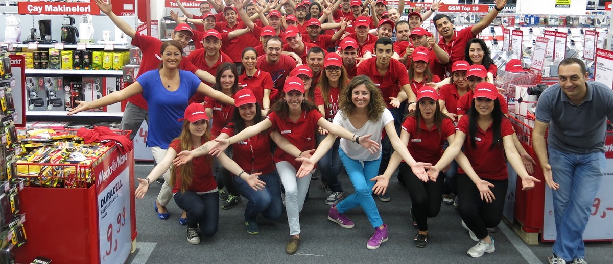 Hande Ermiş and around 40 employees posing in the corridor of a technology outlet after a company event.